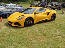 Yellow Lotus Emira in front of other Lotus cars and Land Rovers on a grassy field